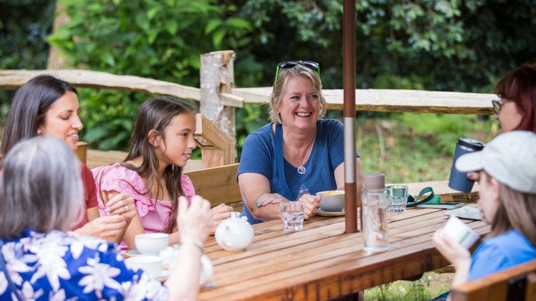 Visitors chatting and having drinks around an outside cafe table at Winkworth Arboretum